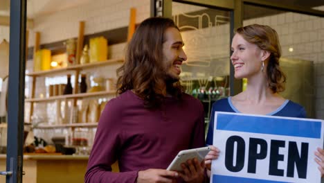 Waiter-and-waitress-with-open-sign-board-standing-at-the-entrance-4k