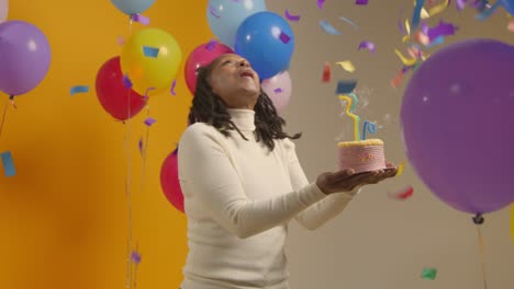 retrato de estudio de una mujer con una cinta para la cabeza de cumpleaños celebrando su cumpleaños soplando velas en el pastel 1