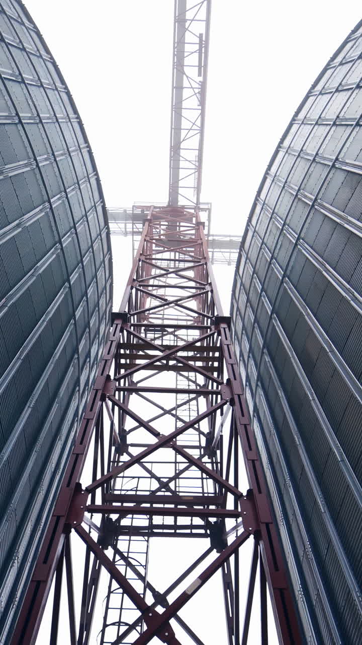 High metal support between two tanks of grain dryer. A walk between the huge tanks right under the metal support. View from below. Vertical video