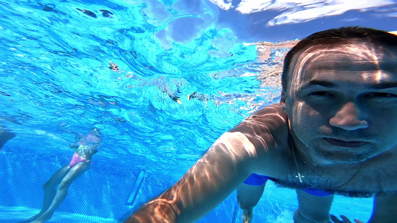 Healthy male is diving in blue water. A man swimming under the clear water with camera inside the pool. Underwater concept.