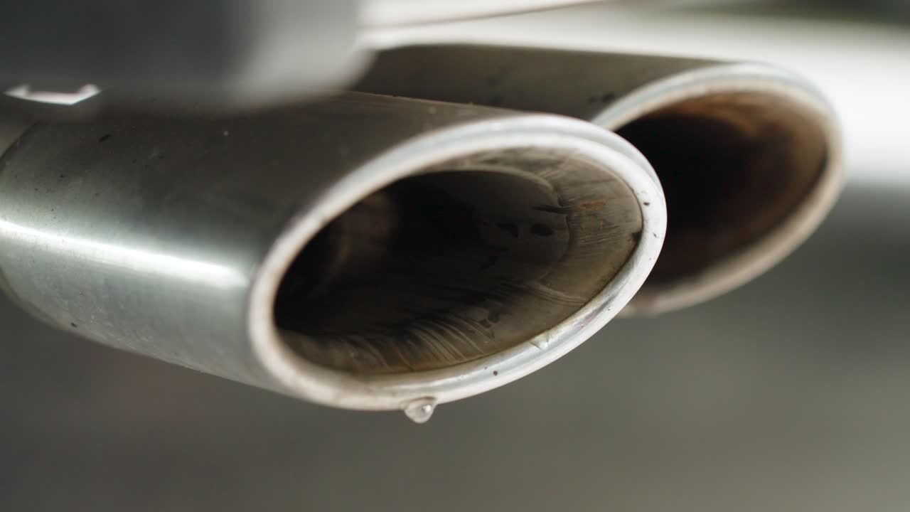 Close-up of a V8 double exhaust with water vapor droplets bursting out. Powerful cinematic shot emphasizing engine force and motion.