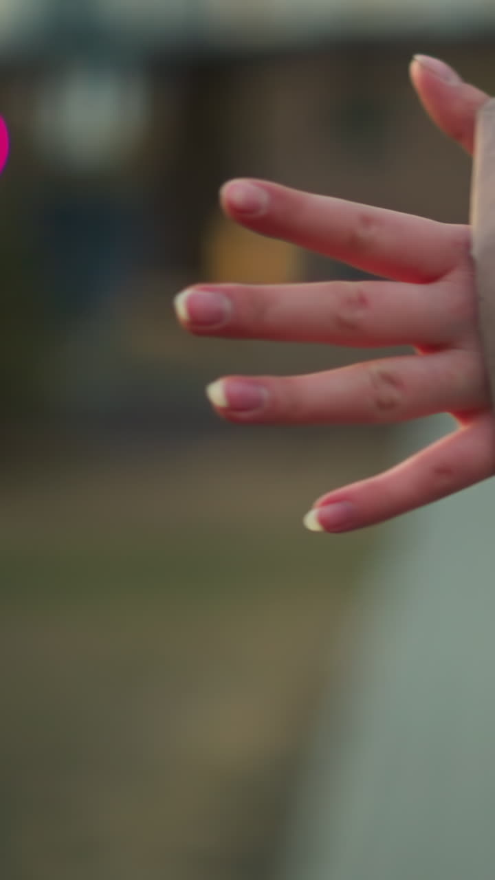 un primer plano captura la mano de una persona en una chaqueta de melocotón, con los dedos extendidos, en un fondo urbano borroso con iluminación suave y efectos bokeh
