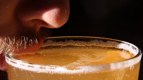 close up of a caucasian male sipping from a tall refreshing glass of beer with a dark backdrop