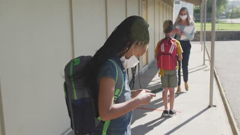 girl wearing face mask using smartphone at school