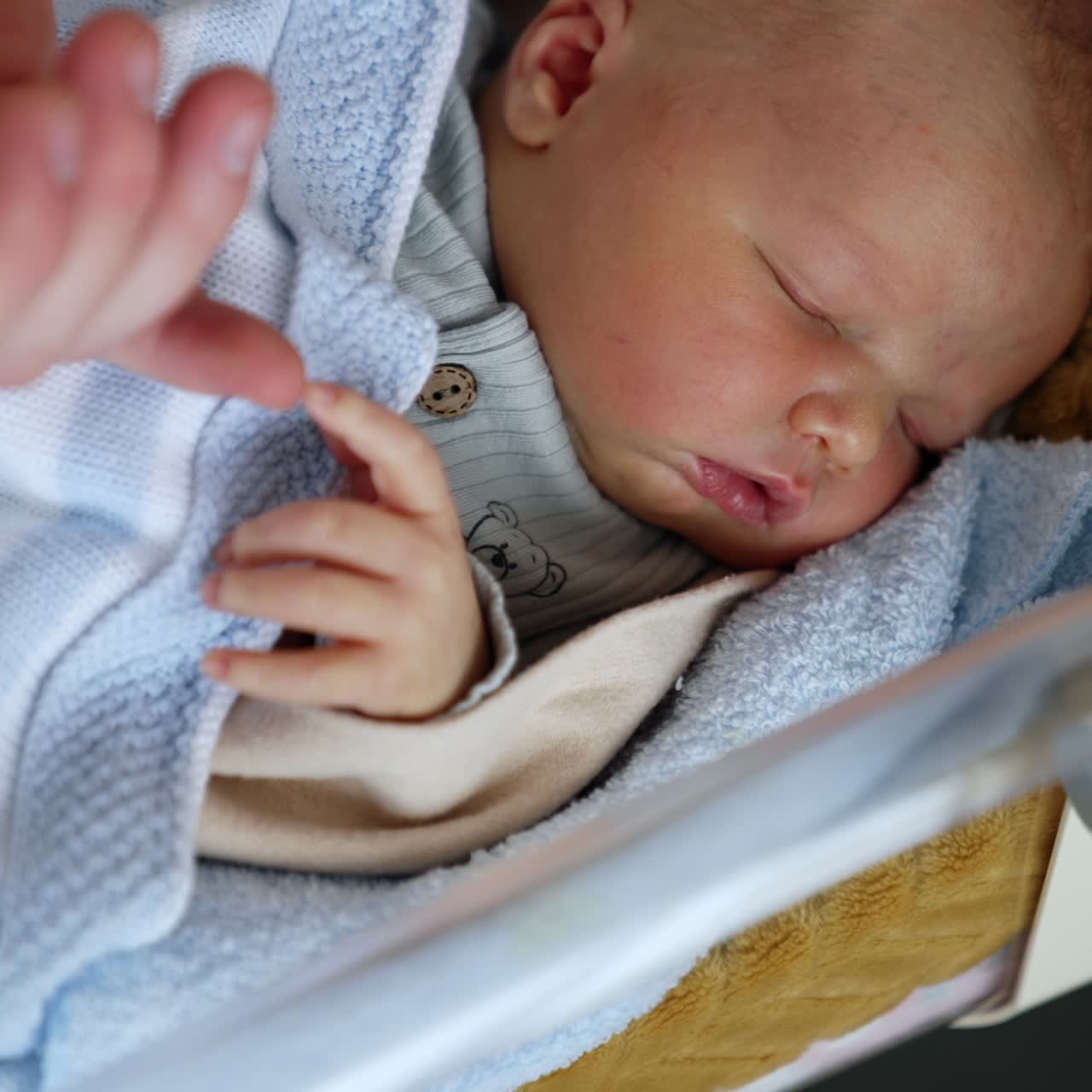 Infant sleeping tight in a little crib. Dad's hand touching cute tiny fingers of a newborn. Close up
