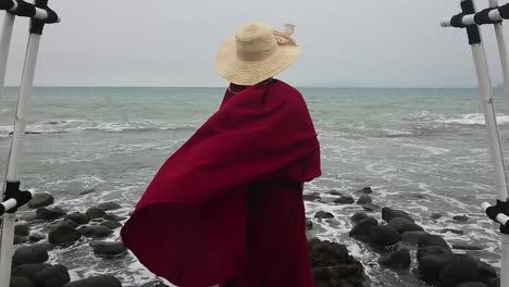 islamic woman wearing burqa during holiday at rocky beach, puts on straw hat