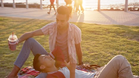 vertical video of diverse gay male couple having picnic at promenade by the sea, slow motion