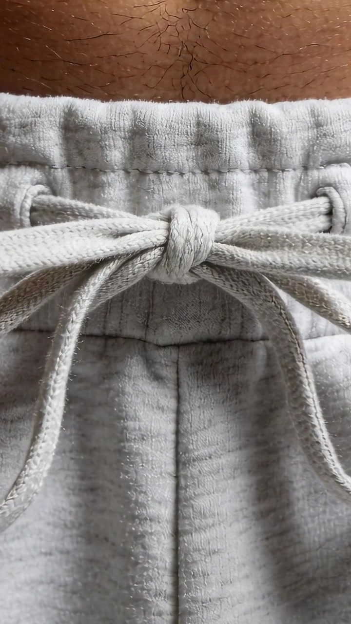 Video verticale: Che mostra un torso che si muove leggermente a casa, con la coulisse che si sposta su pantaloni della tuta grigio chiaro.