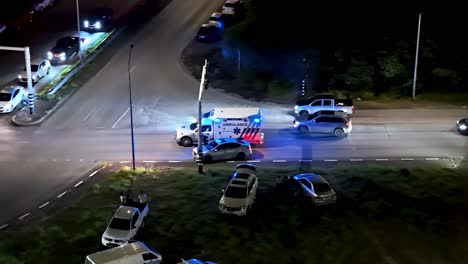 ambulance with flashing blue lights weaves between cars on busy road, aerial drone tracking at night