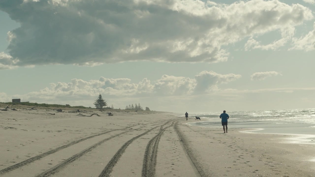People walking on golden sandy beach along lucid shiny ocean water, New Zealand