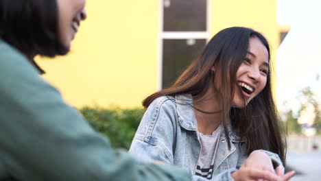 Zwei-Hübsche-Junge-Japanische-Mädchen-Reden-über-Etwas-Lustiges-Und-Lachen,-Während-Sie-Im-Freien-Sitzen