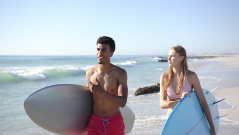 Junger-Biracial-Mann-Und-Kaukasische-Frau-Halten-Surfbretter-An-Einem-Sonnigen-Strand