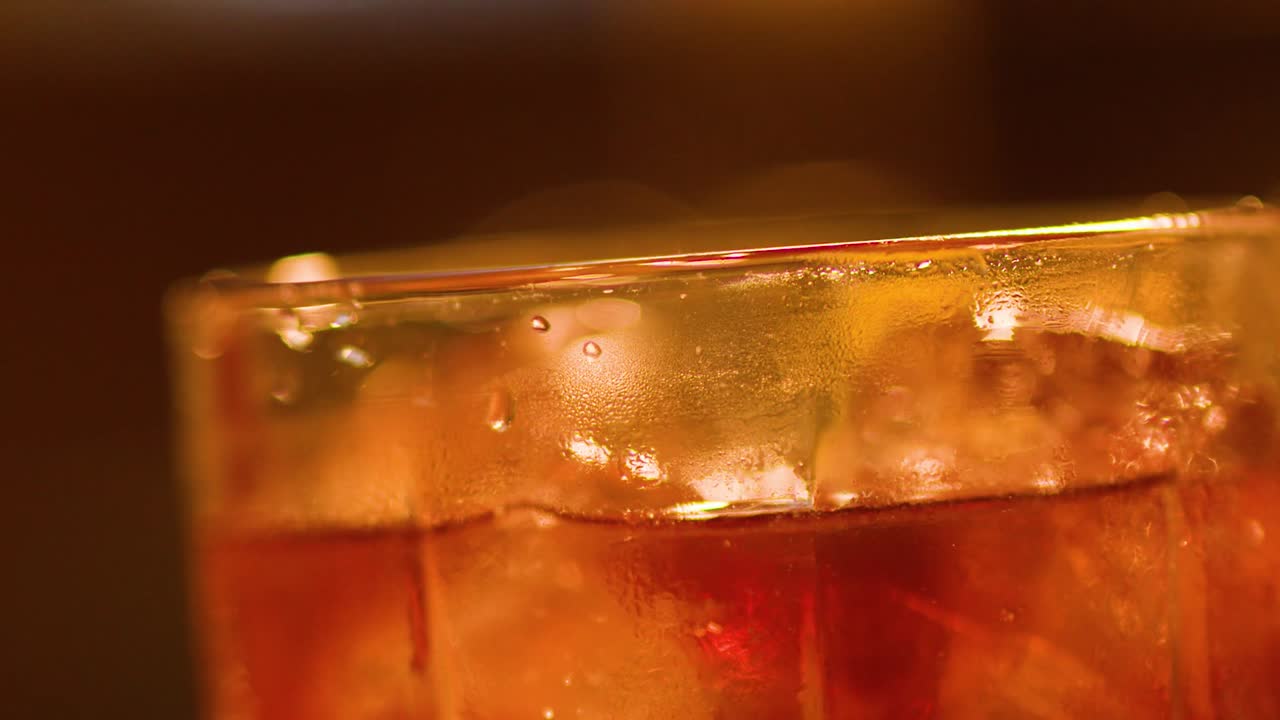 Macro di una bevanda ambrata ghiacciata con cubetti di ghiaccio sotto una calda luce da bar