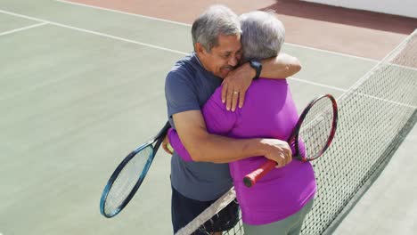 video de una feliz pareja de mayores de dos razas abrazándose en una cancha de tenis