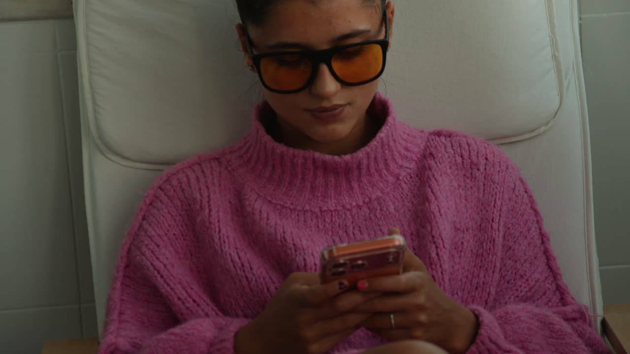Giovane donna con maglione rosa che messaggia sullo smartphone