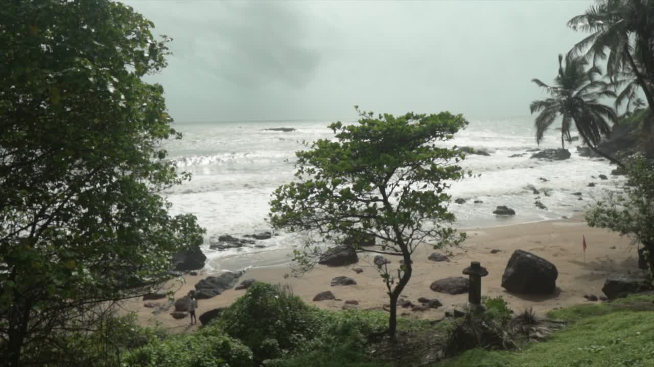 una toma en cámara lenta de las olas del océano rompiendo en la playa del agujero de la abuela, en la distancia se acercan nubes grises de tormenta, goa, india