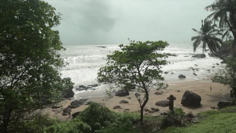 A-slow-motion-shot-of-the-crashing-ocean-waves-at-Grandmother’s-hole-beach,-in-the-distance-grey-storm-clouds-approach,-Goa,-India