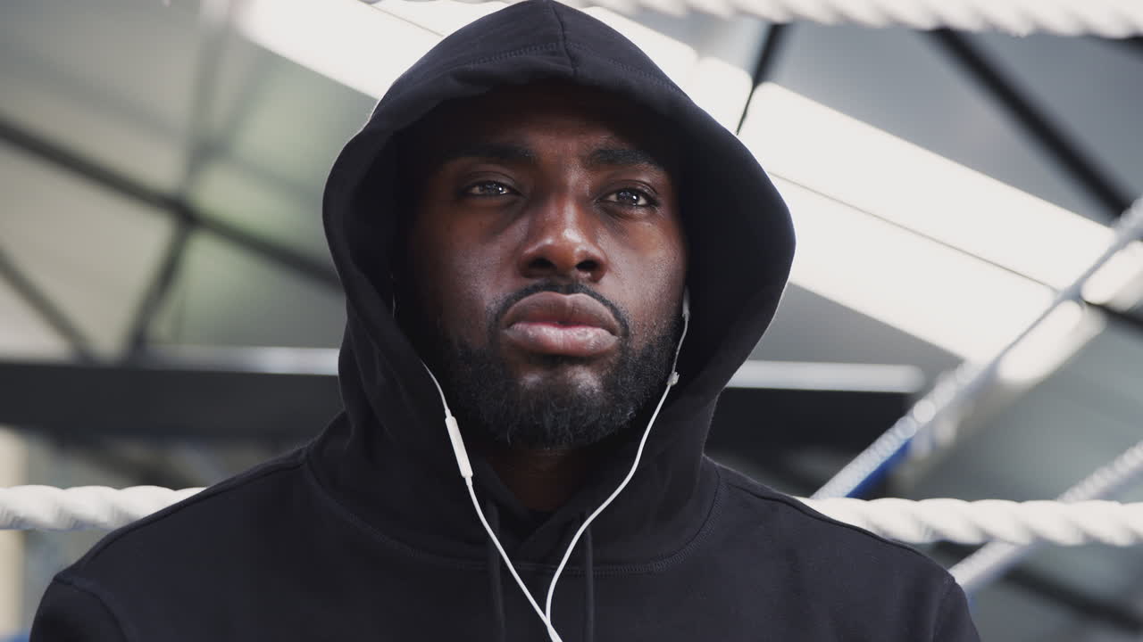 мужской боксер тренируется в спортзале, слушает музыку в наушниках на боксерском ринге.