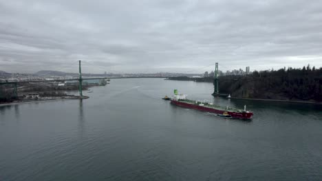 red barge passing under lions gate bridge with vancouver city in background, canada