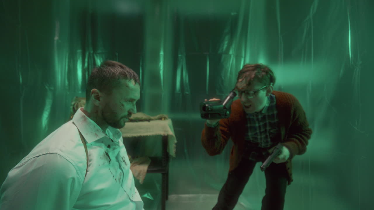 un maníaco con una pistola y filmando a un rehén en una habitación cubierta de plástico