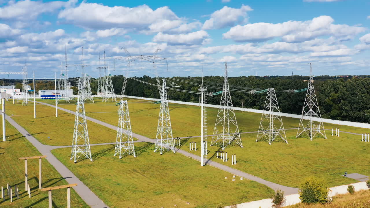 High voltage steel pylons on green field. Power transmission lines at sunlight. White electricity towers in summer day.