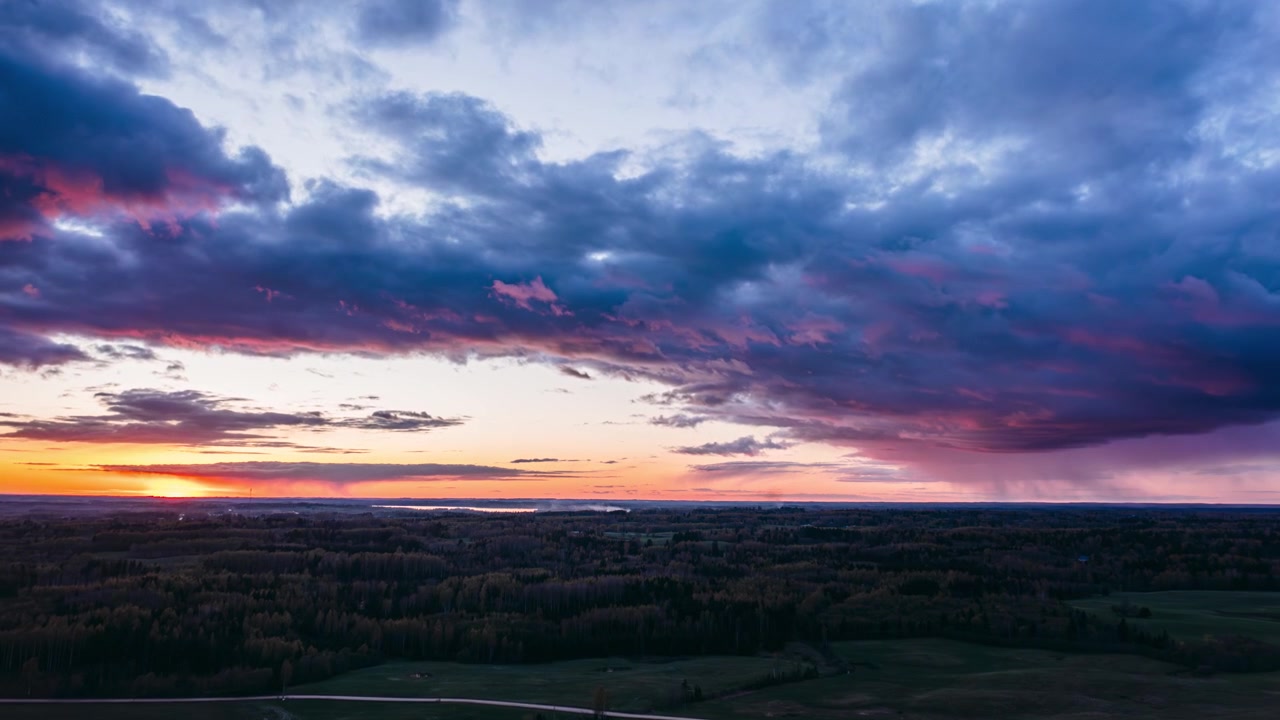 Aerial drone hyperlapse of a vibrant sunset over vast forests and green fields under dramatic clouds. Colorful evening over countryside landscape.