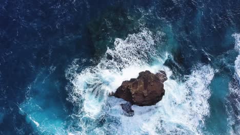 bright deep blue waves crashing on a large sea stack at spitting cave honolulu hawaii - aerial top down static