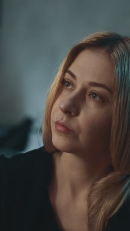 concentrated long haired woman looks at small pill bottle with unregistered nutritional product on blurred background in semi-dark room closeup slow motion