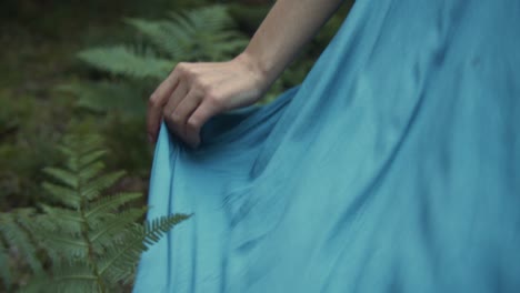 woman holding her blue dress walking in the forest like a fairy, close up