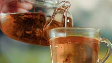 pouring tea from a glass teapot into a clear teacup