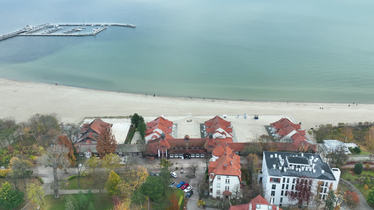 Aerial view of Sopot coastline with sandy beach, red-roofed resort buildings, and Baltic Sea during autumn