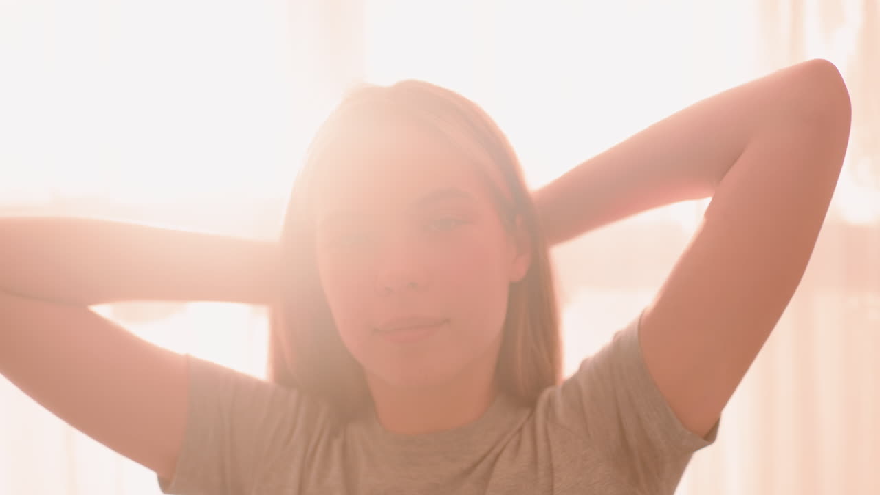 Close up of woman stretching shoulder with eyes closed in peaceful expression, arms raised overhead, soft sunlight filtering through curtains highlighting calm relaxed moment of wellness and balance