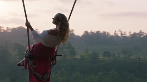 happy-woman-swinging-over-tropical-rainforest-at-sunrise-sitting-on-swing-with-scenic-view-enjoying-freedom-on-vacation-having-fun-holiday-lifestyle-slow-motion