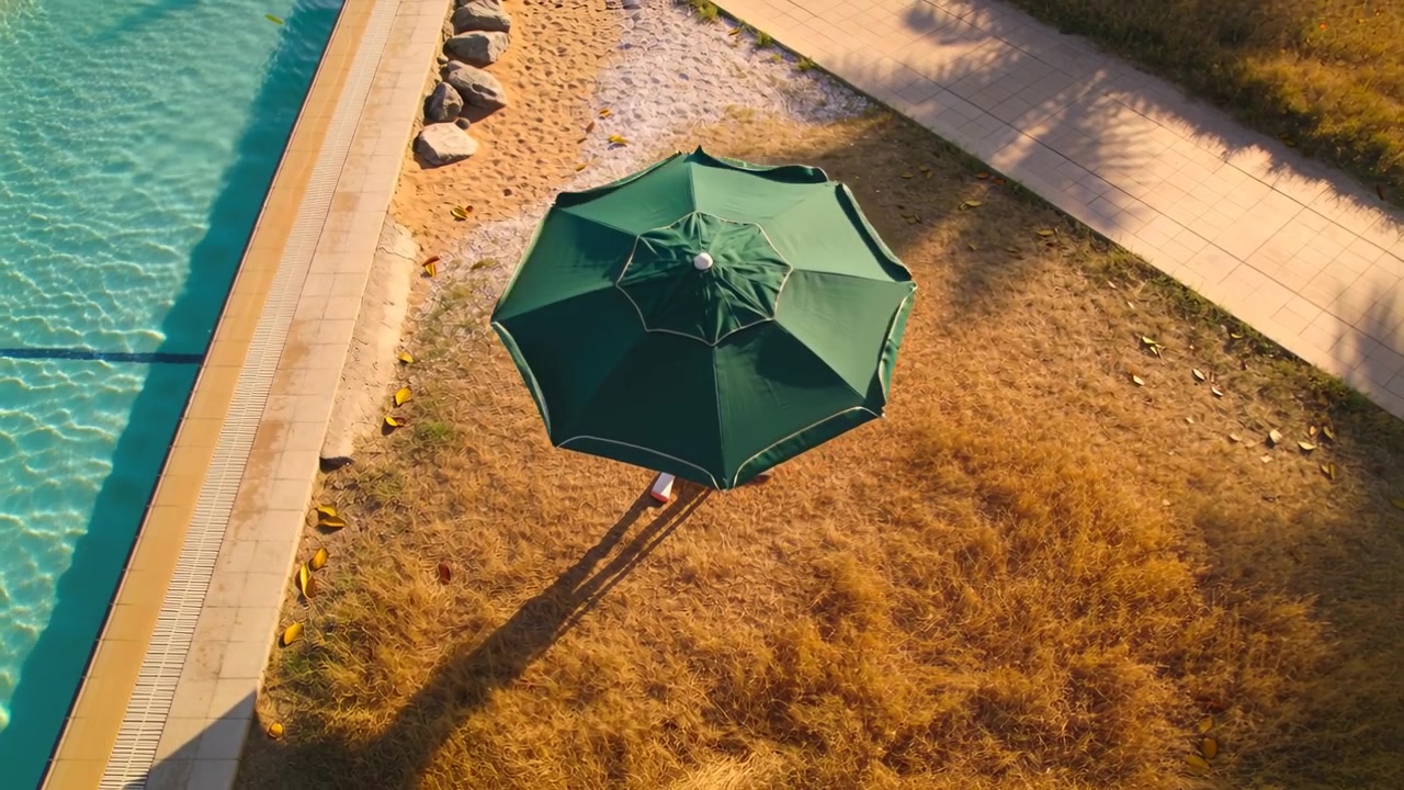 Drone che si sposta, rivelando un ombrellone ottagonale verde a bordo piscina, con una persona in piedi che indossa pantaloncini rossi.