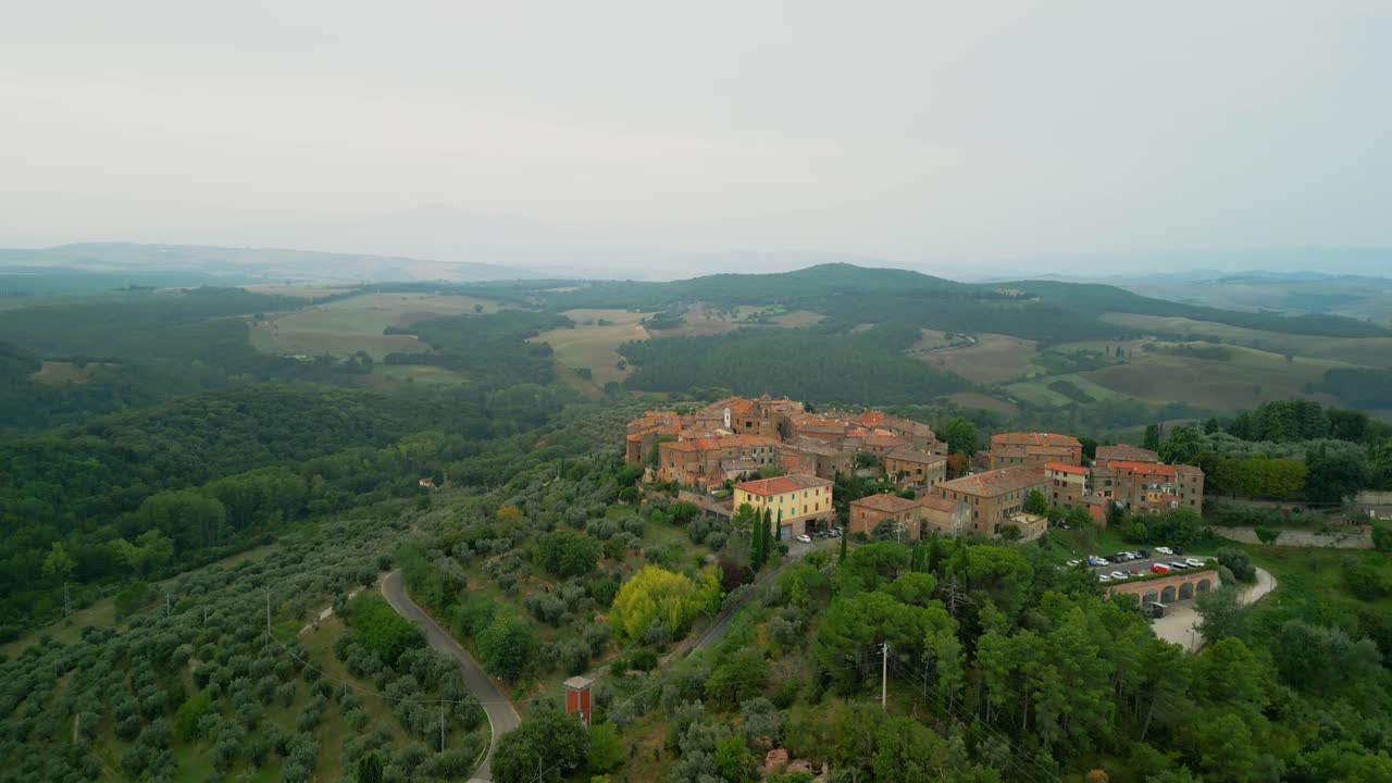 Sunrise light touches Tuscan hill town rooftops and countryside in atmospheric aerial scene