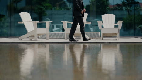 Man-in-a-black-suit-walking-by-a-reflective-water-surface-with-white-chairs-in-the-background