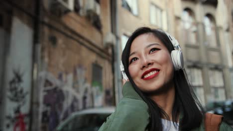 Close-Up-Of-The-Young-Charming-And-Happy-Stylish-Woman-In-Headphones-Going-The-Street-In-Slums-And-Listening-To-The-Music-Cheerfully