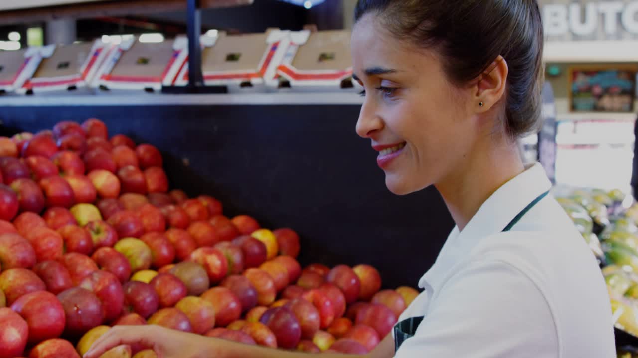 Female produce clerk spotting misaligned apples and reordering fruit while checking quality