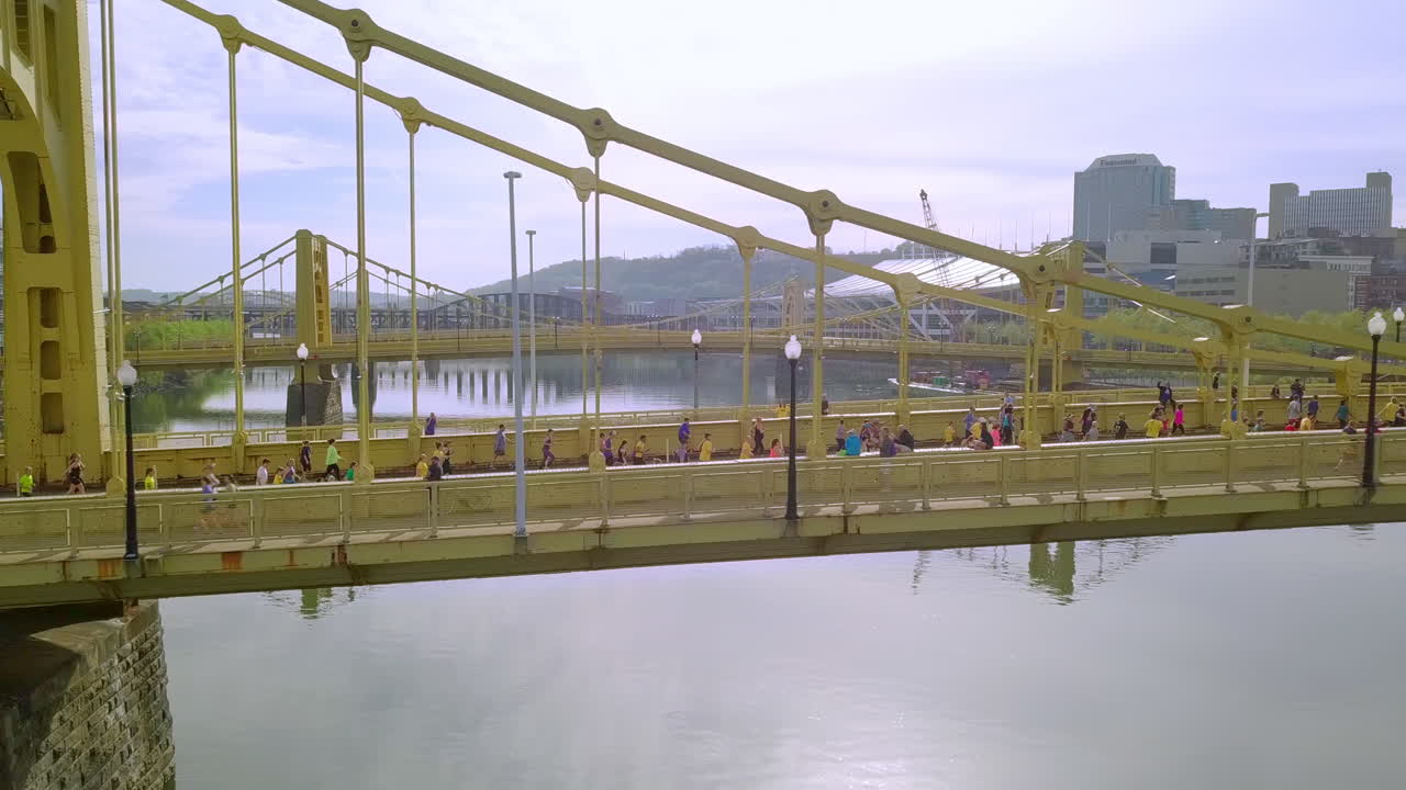 Aerial follow shot of runners crossing bridge, Pittsburgh Marathon.