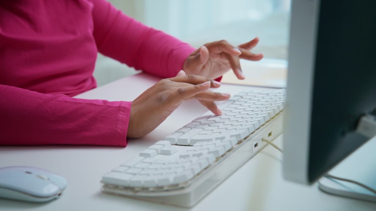 Professional female worker wearing pink shirt typing efficiently on white keyboard in modern, bright office workspace during productive workday