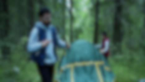 Blurred-shot-of-couple-setting-up-a-tent-while-camping-in-the-woods,-natural-surviving-concept