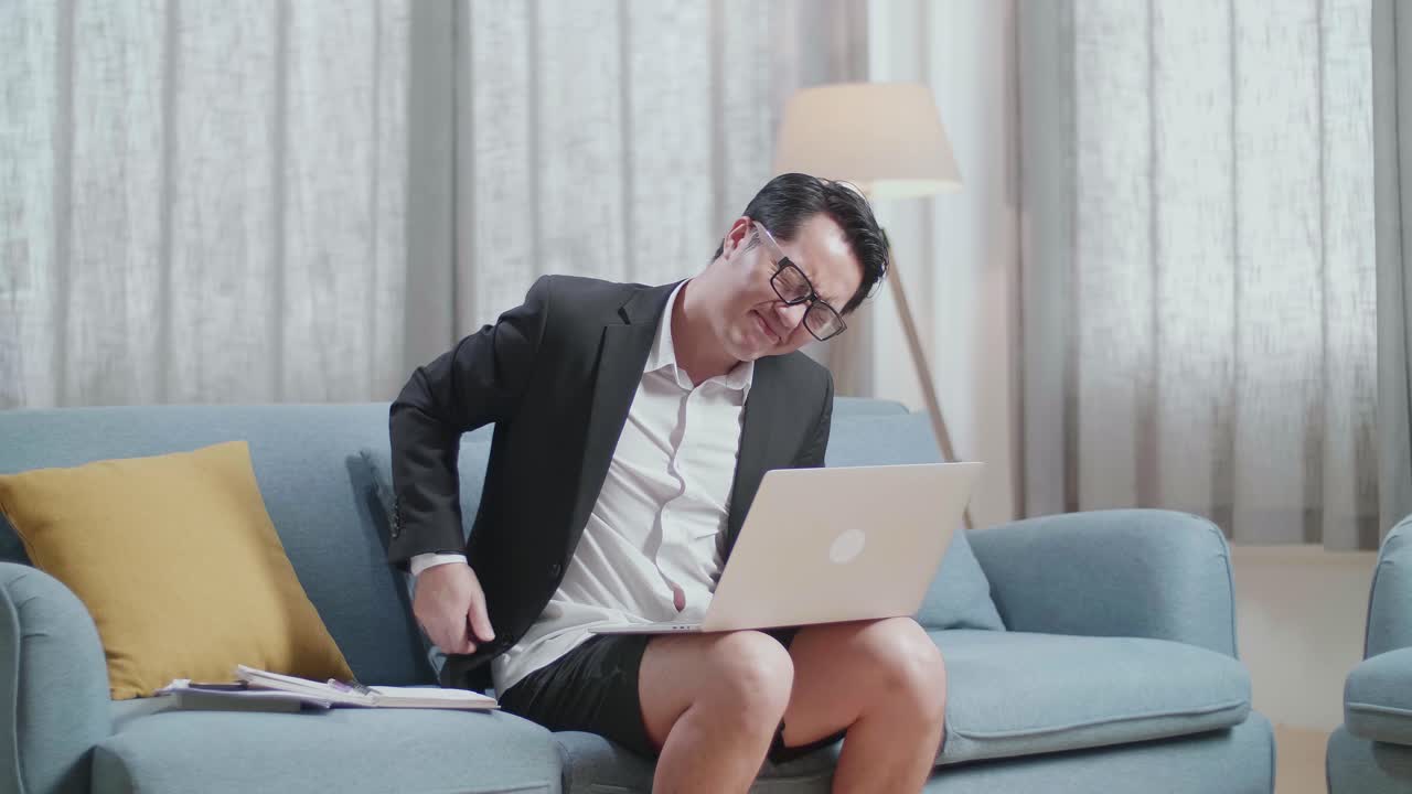 자켓과 쇼트 입은 아시아 사업가 가 집 에서 노트북 을 사용 하면서 허리 통증 을 겪고 있다
