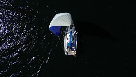 From-an-aerial-perspective,-a-sailboat-gracefully-appears-with-its-vibrant-sail,-gliding-on-the-dark-waters-of-the-Baltic-Sea