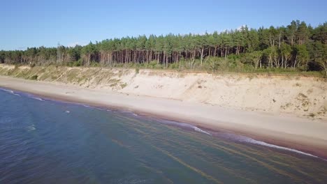 Aerial-view-of-Baltic-sea-beach-at-Jurkalne-on-a-sunny-day,-white-sand-cliff-damaged-by-waves,-coastal-erosion,-climate-changes,-wide-angle-drone-shot-moving-forward-high