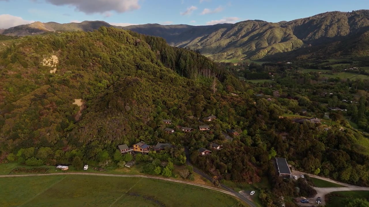 Vista aerea con drone che si affaccia su case sulla lussureggiante collina verde ai margini della città di Marahau, Area di Abel Tasman, Nuova Zelanda.