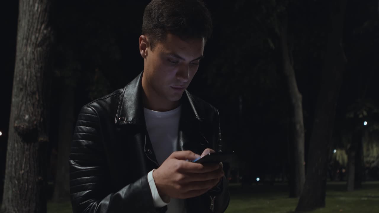 밤 에 공원 에서 전화 를 사용하는 젊은 남자