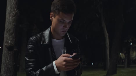 young man using phone in a park at night