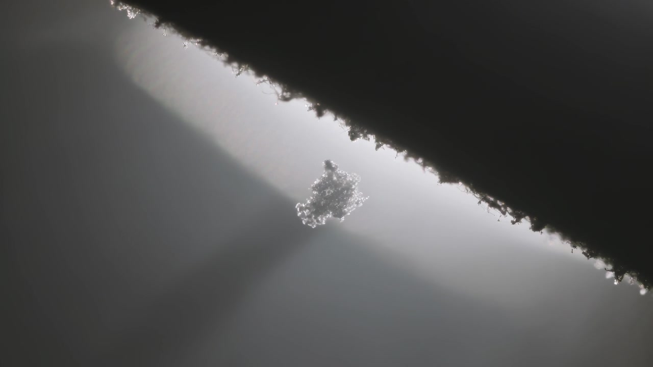 Detaching translucent flake descending in backlit macro, textured diagonal rim releasing fragment