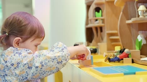 korean-ukrainian 2-year-old toddler girl playing with toy figures in dollhouse sitting by the desk