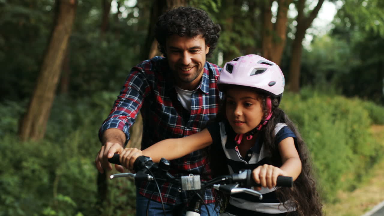Closeup. Portrait of a little girl and her father. Dad teaching his daughter to ride a bike. Lets her go. Moving camera. Blurred background